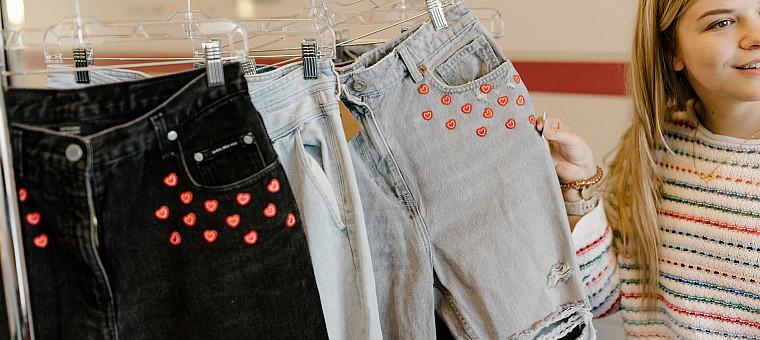 Jeans with red hearts around the pockets hang on a rack.